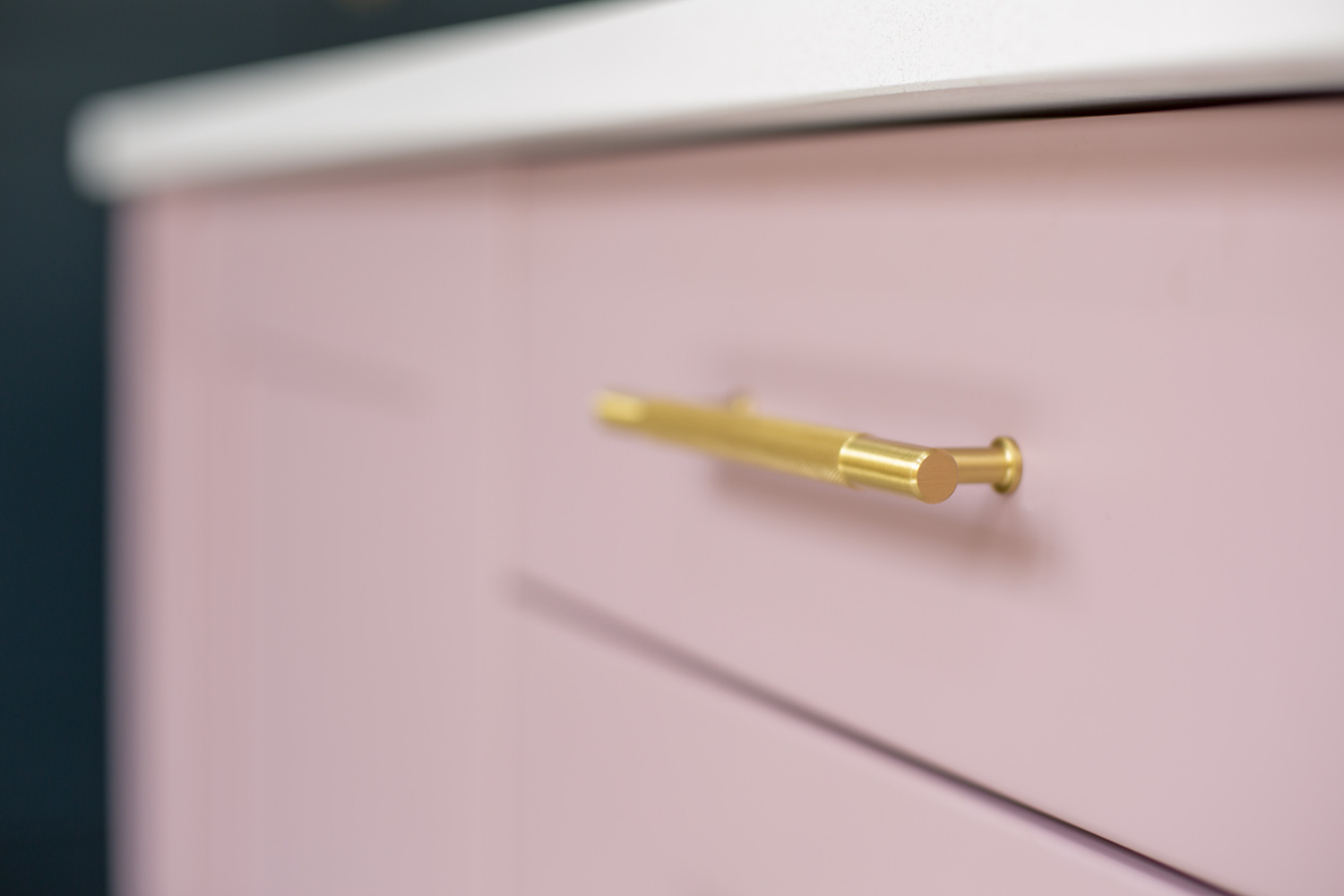 A close up of a pink kitchen cabinet with a beautiful gold handle